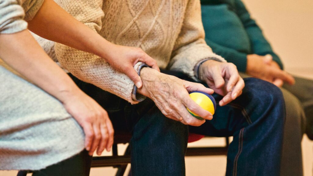 Service user with dementia sitting at home with a SWL Care Haven carer, holding a soft exercise ball during a supportive activity.